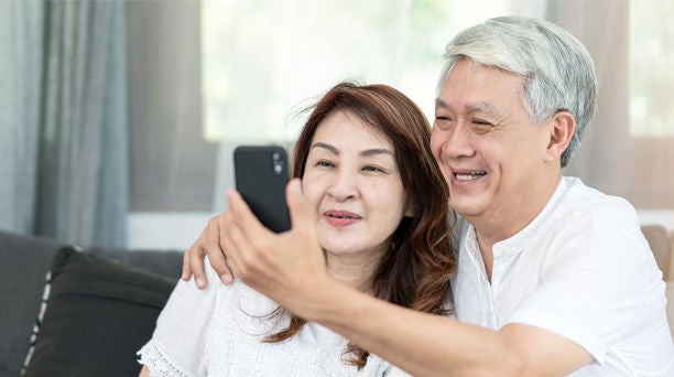 Old Asian couple smiling and doing a video call on phone.
