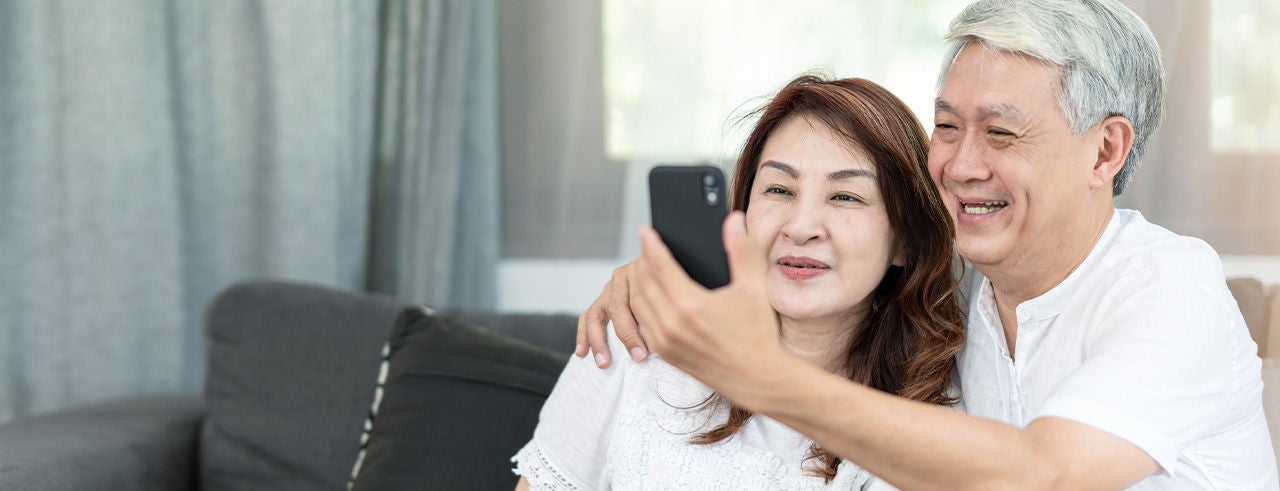 Old Asian couple smiling and doing a video call on phone.