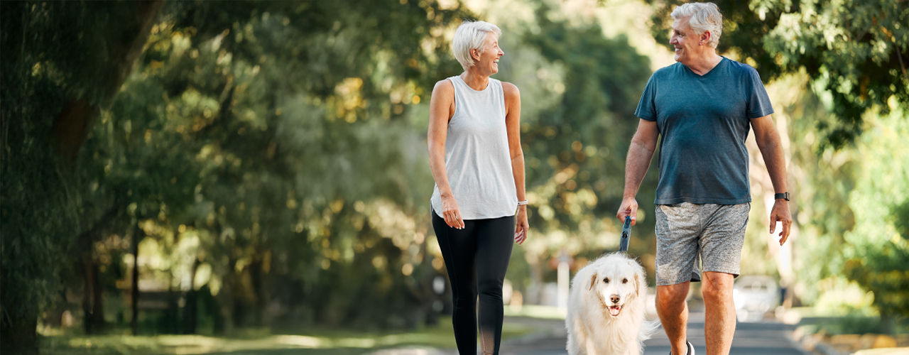 Old couple smiling and walking inside a park with dog.