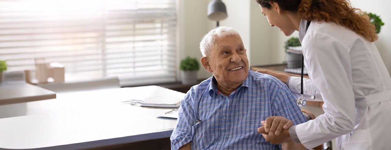Female physican holding hand of old male patient and consulting him.
